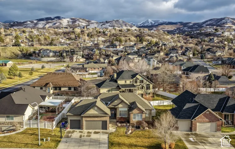 Aerial view featuring a multi-level residential exterior with brick and siding facade, an asphalt shingle roof, an attached multi-car garage, a concrete driveway, and mountain range scenery