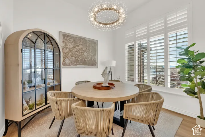 Dining area featuring wood-finish flooring, white plantation shutters, and a circular crystal chandelier