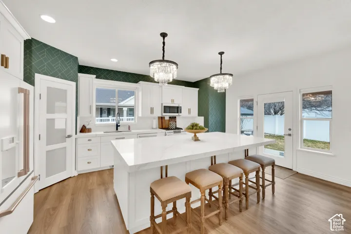Kitchen featuring white shaker-style cabinetry, quartz countertops with a waterfall edge island, geometric patterned accent walls, crystal chandelier lighting, and wood-finish flooring