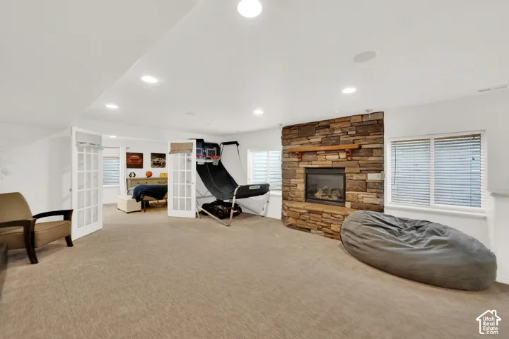 Floor-to-ceiling stone fireplace featuring a wood mantel, recessed lighting, carpeted flooring, and French doors