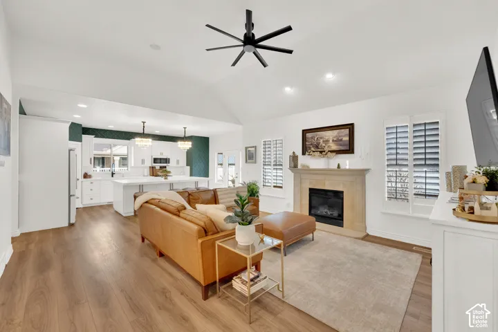 Open-concept interior featuring vaulted ceilings, wood-finish flooring, a stone-surround fireplace, plantation shutters, and a kitchen island with pendant lighting