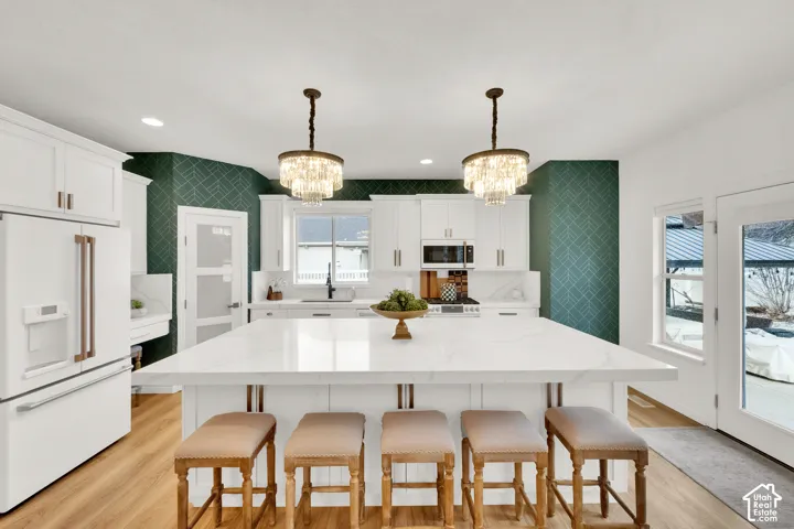 Kitchen featuring a large central island with a quartz countertop, white cabinetry, dual tiered crystal pendant lighting, and geometric-patterned accent walls