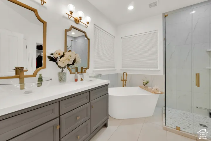 Dual vanity with glass vessel sinks, quartz countertops, and brass fixtures, accompanied by a freestanding soaking tub and a walk-in glass-enclosed shower with tile surround