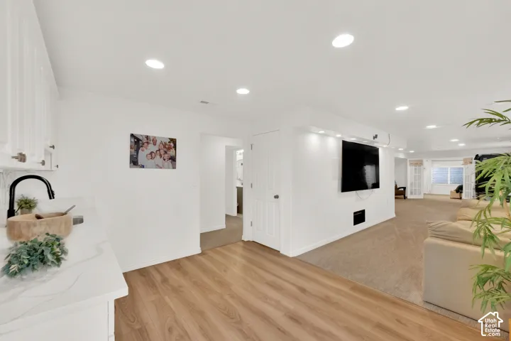 Interior space featuring wood-finish flooring, recessed lighting, white cabinetry with stone-surface countertops, matte black faucet, and a wall-mounted media feature