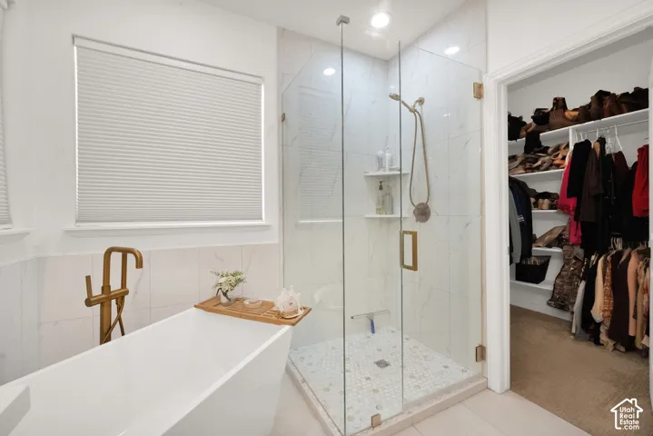 Freestanding soaking tub with a floor-mounted brass faucet, walk-in glass-enclosed shower with tiled walls, mosaic floor tile, and built-in closet shelving