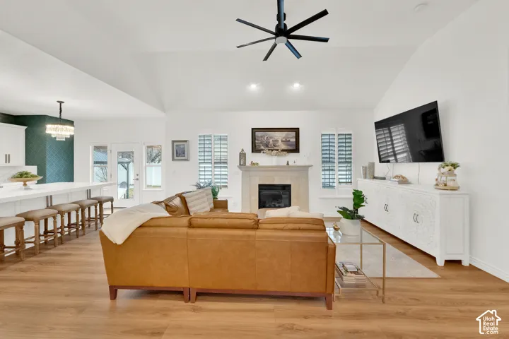 Vaulted ceiling with a matte black modern ceiling fan, wood-finish flooring, stone-surround fireplace with a mantel, and plantation shutters