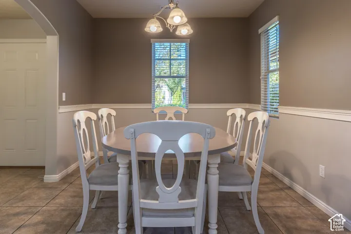 Tile flooring, neutral wall color with wainscoting, and multi-light chandelier fixture