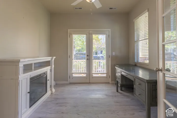 Room featuring light-toned wood-finish flooring, built-in cabinetry with an integrated electric fireplace, dual-pane French doors with horizontal blinds, and a ceiling fan