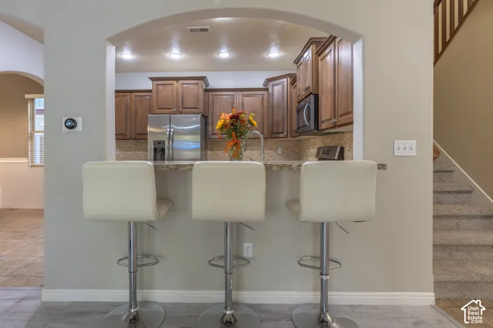 Kitchen featuring an arched pass-through window, wood cabinetry, stone-surface countertop, recessed ceiling lighting, and stainless steel appliances