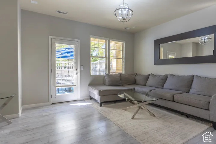 Light-toned wood-finish flooring, full-light glass door, dual windows with blinds, orb-style chandelier, and large wall-mounted mirror