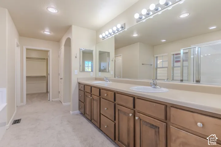 Double vanity featuring wood cabinetry, integrated sinks, a full-width wall mirror, and dual multi-bulb light fixtures