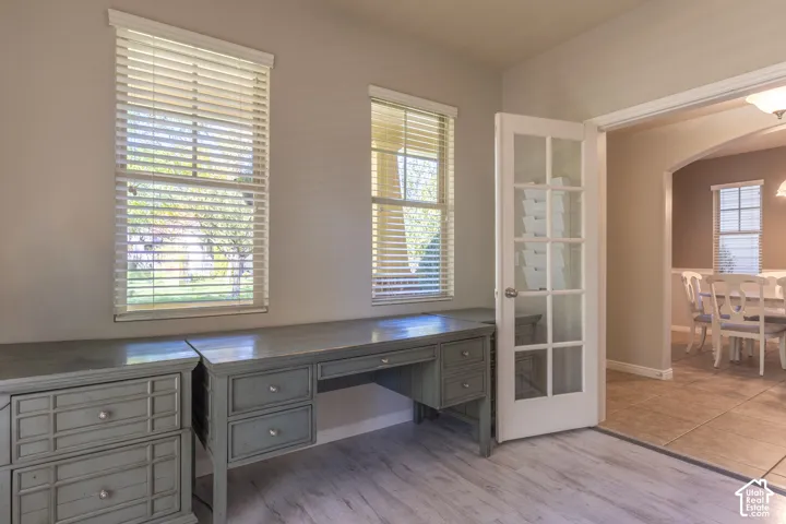 Built-in cabinetry with integrated desk space, wood-finish flooring, dual windows with horizontal blinds, and a glass-paneled French door