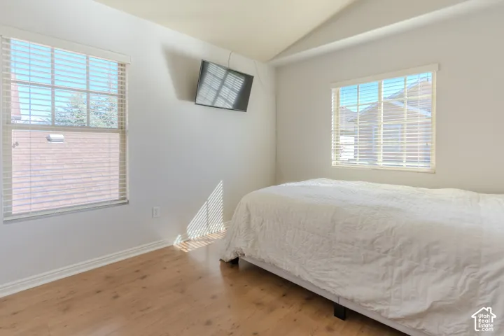 Vaulted ceiling, wood-finish flooring, and dual windows with fitted blinds