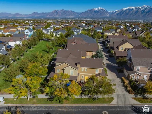 Aerial perspective featuring a two-story residence, asphalt shingle roofing, exterior stucco siding, mature deciduous trees, and a mountain range backdrop
