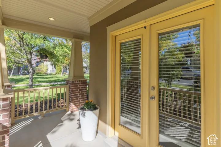 Covered front porch featuring a brick-based tapered column, beadboard ceiling, wood-style railing, and glass-paned double entry doors