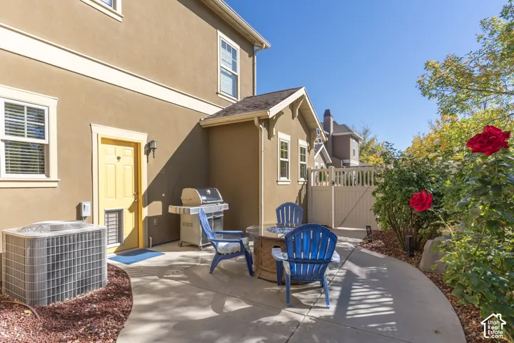 Rear concrete patio featuring integrated landscaping with rose bushes, decorative stone ground cover, and a solid-panel privacy gate