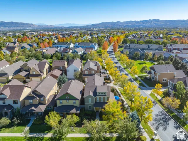 Aerial perspective of a residential neighborhood featuring paved streets, established tree-lined landscaping, manicured lawns, and a mountainous horizon