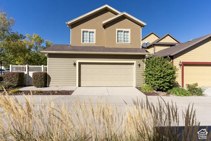 Two-story exterior featuring tan horizontal siding, a double-car garage, multi-pane windows, and a shingled roof