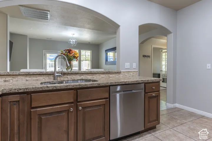 Kitchen featuring stained wood cabinetry, stone-finish countertops, stainless steel dishwasher, undermount sink with gooseneck faucet, and architectural arched doorways
