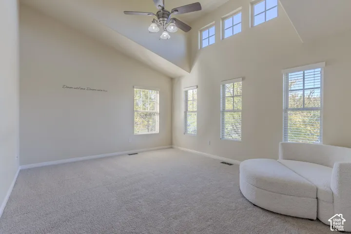 Vaulted ceiling, multiple levels of windows, wall-to-wall carpeting, and a ceiling fan with integrated lighting
