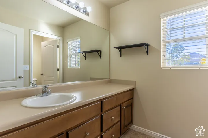 Bathroom vanity featuring wood-finish cabinetry, a solid-surface countertop with an integrated basin, a large wall-mounted mirror, and horizontal window blinds