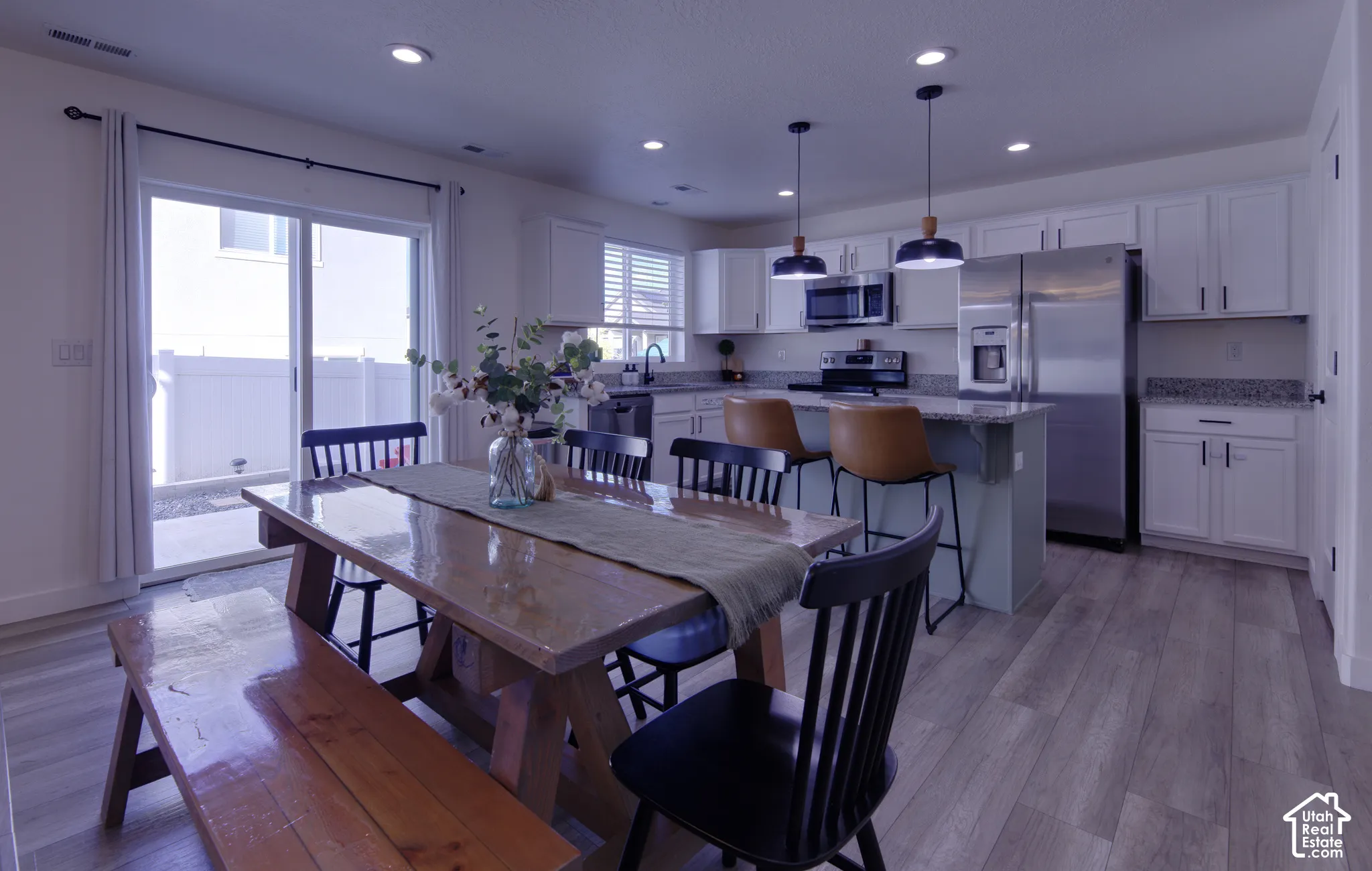 Kitchen featuring white cabinetry, stone-surface countertops, stainless steel appliances, wood-finish flooring, and pendant lighting