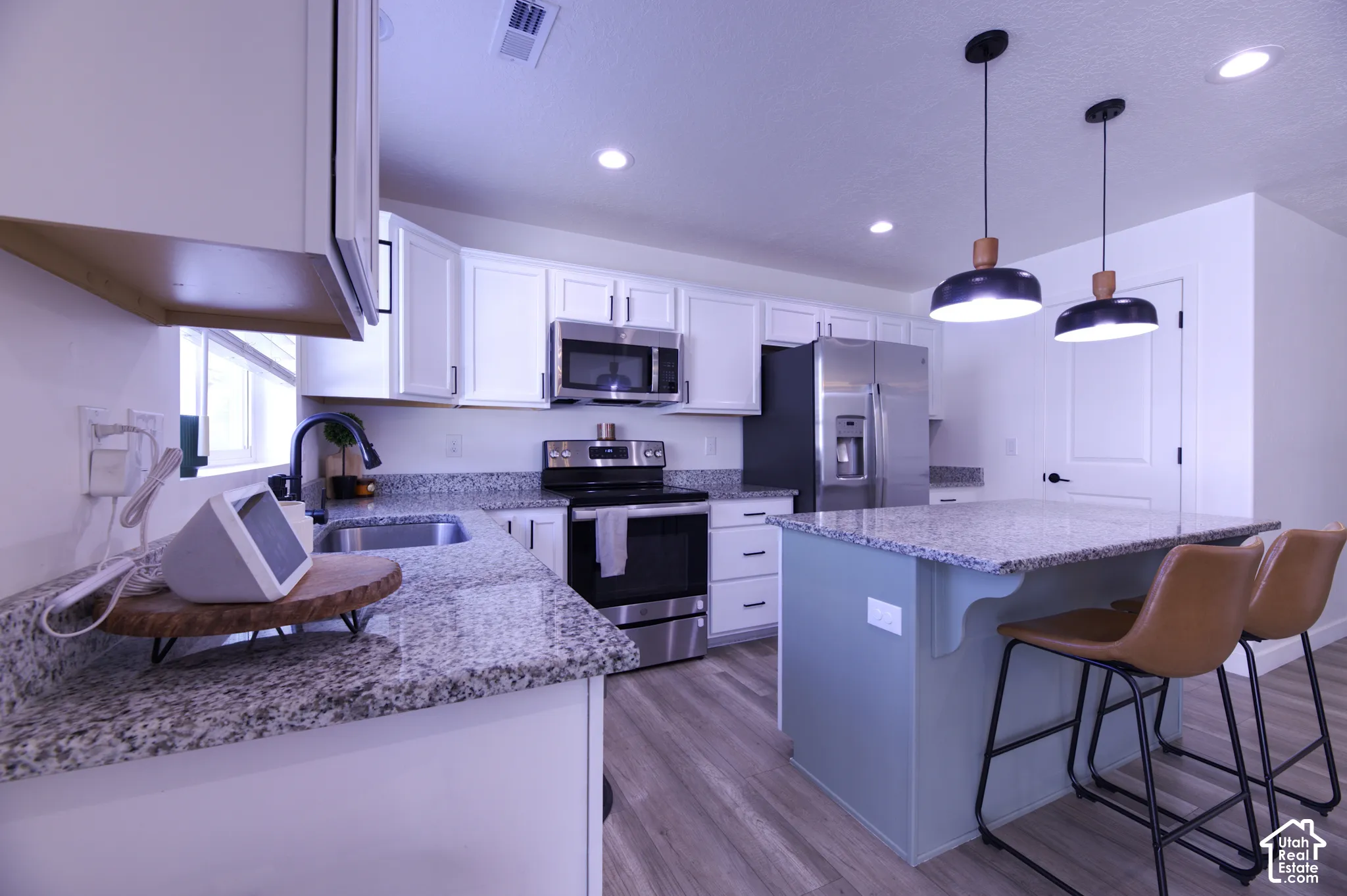 Kitchen featuring white cabinetry, stone-surface countertops, center island with painted cabinetry, stainless steel appliances, and recessed lighting