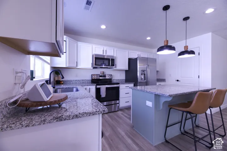 Kitchen featuring white cabinetry, stone-surface countertops, center island with painted cabinetry, stainless steel appliances, and recessed lighting