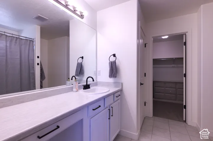 Primary Bathroom vanity featuring a light-toned countertop, integrated basin, matte black hardware, and an expansive wall-to-wall mirror with mounted light fixture