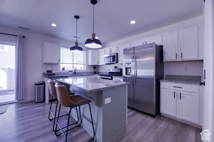 Kitchen featuring white cabinetry, stone countertops, stainless steel appliances, a central island, and wood-finish flooring