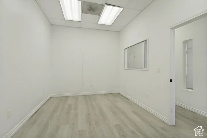 Room featuring wood-finish flooring, drop ceiling with integrated rectangular lighting, and a wall-mounted rectangular mirror