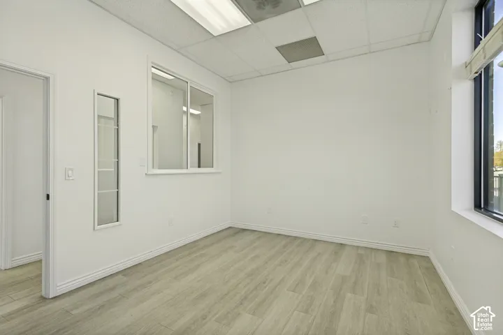 Interior space featuring wood-finish flooring, drop ceiling with recessed lighting, large window with integrated blinds, and a fixed glass partition