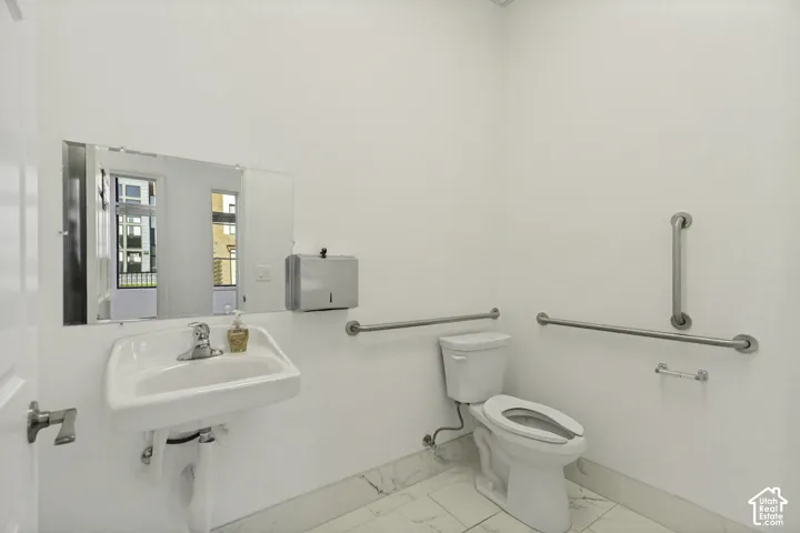 Wall-mounted porcelain sink with chrome faucet, stainless steel grab bars, and polished stone-finish floor tiling