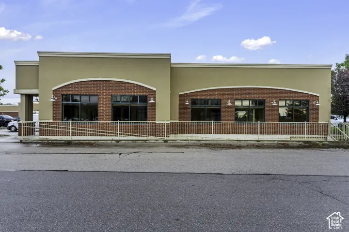 Commercial exterior featuring a tan stucco finish, red brick accents, multi-pane windows with arched brick headers, and exterior gooseneck lighting