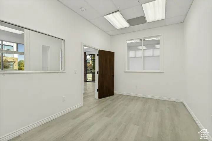 Interior space featuring wood-finish flooring, a solid wood door, integrated wall window panels, and a drop ceiling with recessed lighting
