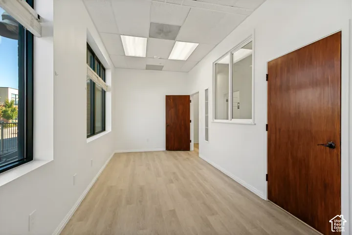 Interior room featuring wood-finish flooring, drop ceiling with recessed lighting, large windows, and solid wood-finish doors