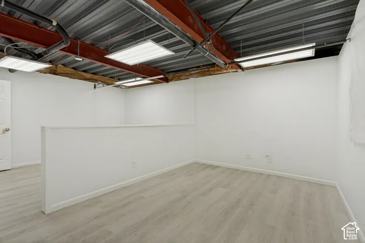 Open-concept space featuring wood-finish flooring, exposed red steel structural beams, metal corrugated ceiling, and suspended rectangular light fixtures