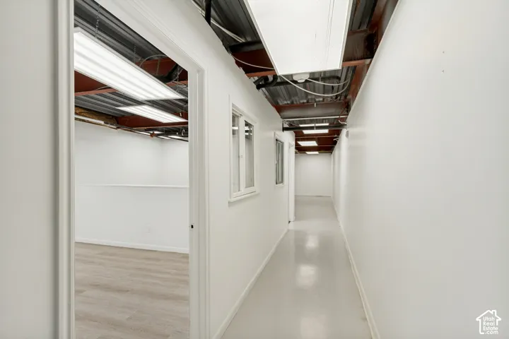 Hallway featuring wood-finish flooring, exposed industrial ceiling, white walls, and interior windows