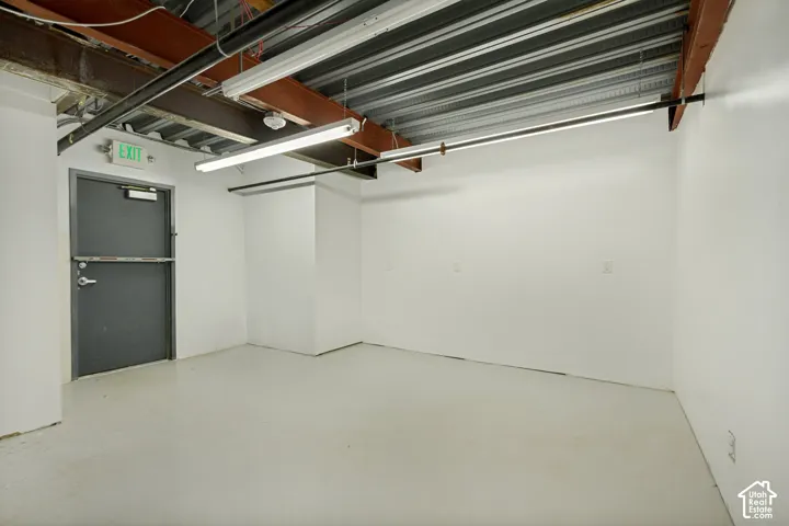 Industrial-style room featuring exposed steel ceiling beams, corrugated metal ceiling, smooth-finish concrete flooring, and linear fluorescent lighting