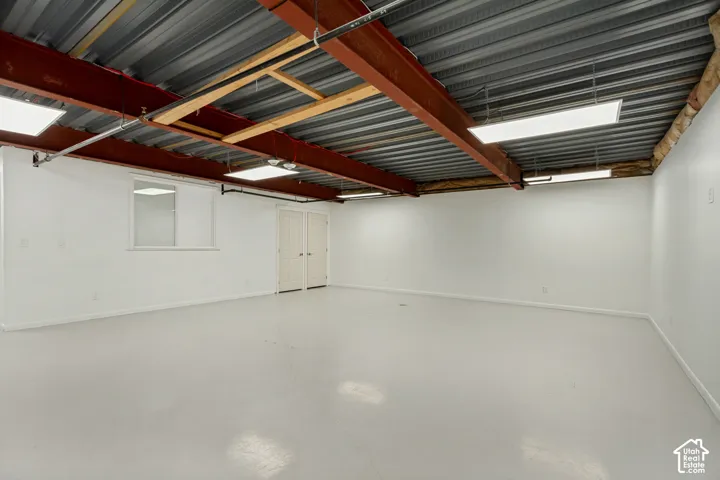 Industrial-style space featuring exposed red steel structural beams, metal corrugated ceiling decking, polished concrete flooring, and recessed rectangular LED panel lighting