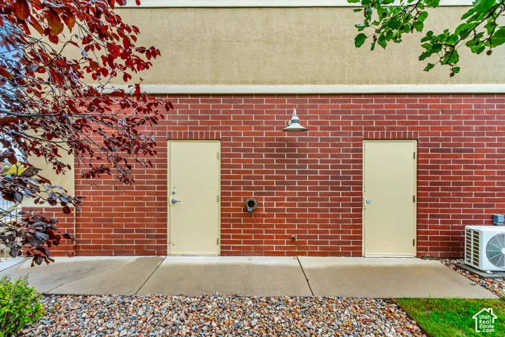 Exterior facade featuring red brick masonry, smooth stucco siding, two steel service doors, a wall-mounted industrial-style light fixture, and a concrete pathway