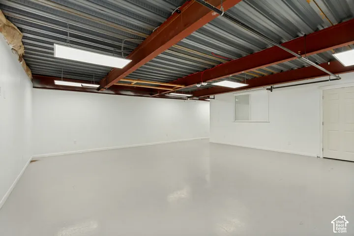 Expansive interior space featuring high-contrast steel structural beams, corrugated metal ceiling, recessed LED panel lighting, and smooth-finish flooring