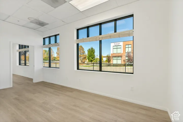 Interior space featuring wood-finish flooring, large multi-pane windows with black frames, drop ceiling panels, and neutral wall tones