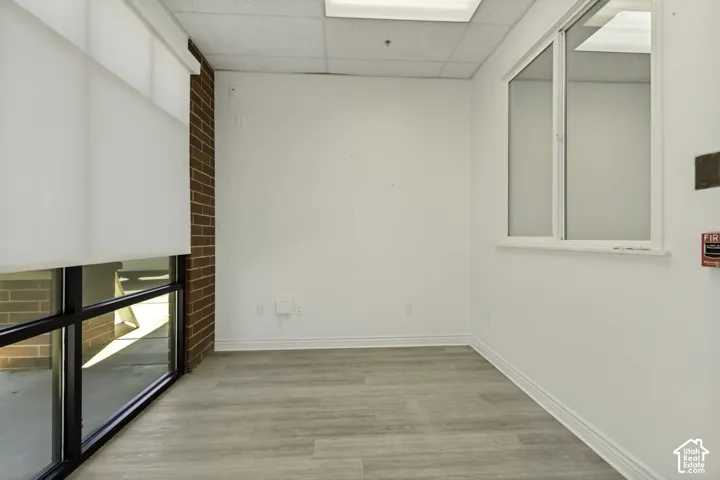 Interior space featuring a brick accent wall, wood-finish flooring, floor-to-ceiling windows with roller shades, and an interior window partition