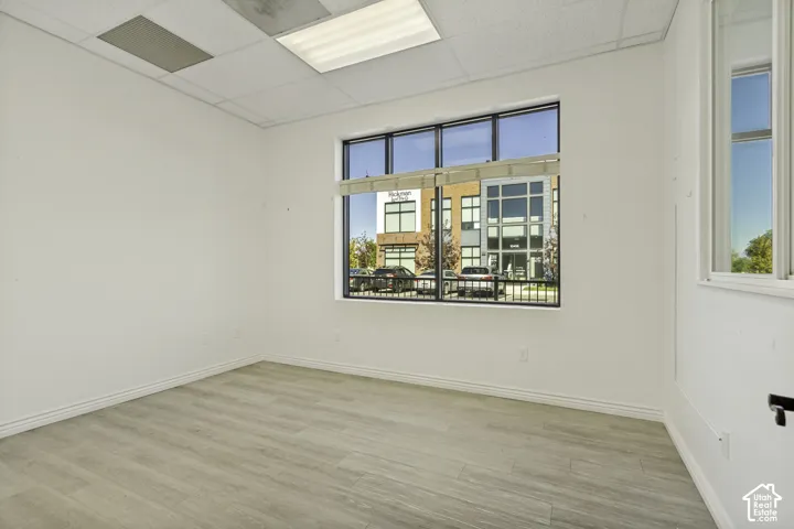 Interior space featuring wood-finish flooring, white walls, a large multi-pane window with a horizontal blind, and a drop ceiling with recessed lighting