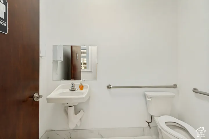 Wall-mounted ceramic sink with chrome faucet, frameless mirror, and dual stainless steel grab bars