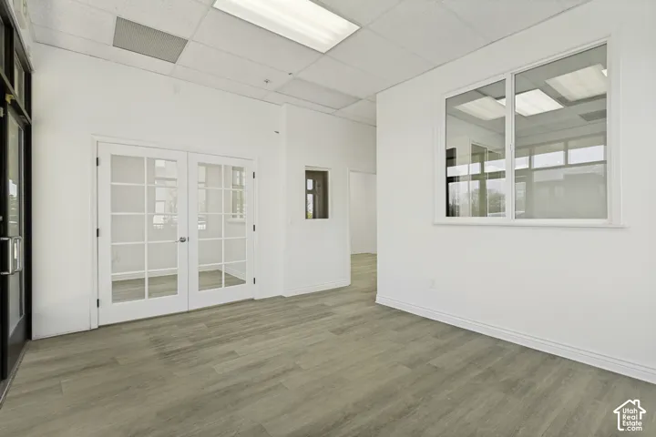 Interior space featuring wood-finish flooring, white walls, drop ceiling panels with recessed lighting, interior glass-paneled double doors, and a large interior glass window partition