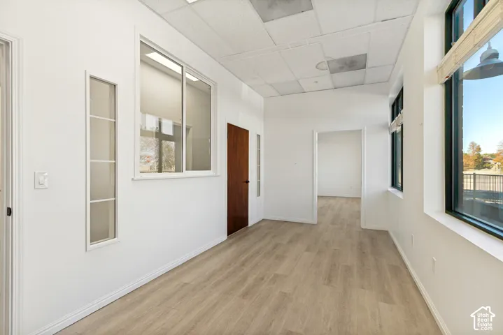 Interior space featuring wood-finish flooring, drop ceiling panels, multi-pane windows, and a dark wood interior door