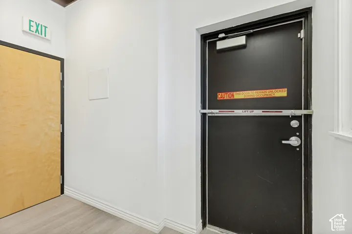 Interior space featuring wood-finish flooring, a light-toned wooden door, and a black steel security door equipped with a horizontal panic bar and an overhead door closer
