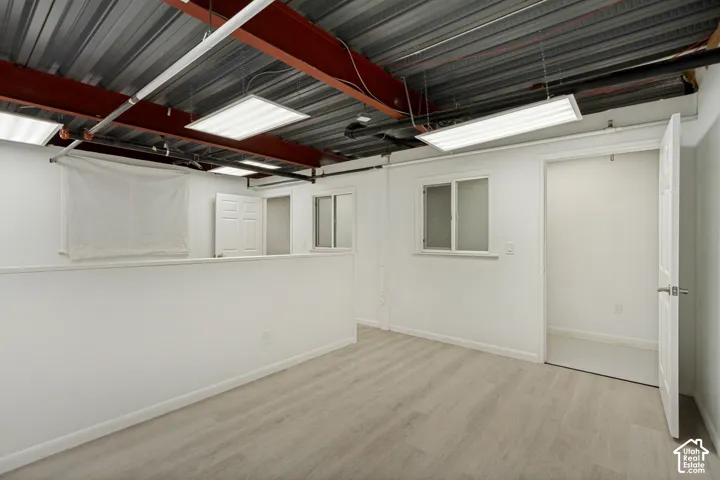 Industrial-style space featuring a high-exposed ceiling with steel beams, neutral wood-finish flooring, recessed-panel doors, and multiple surface-mounted light fixtures